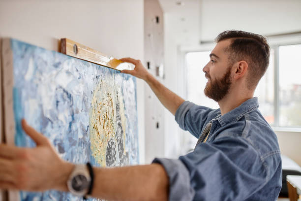 istock Man with beard hanging a painting on the wall at his living room 1312339708