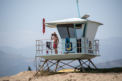 Ventura, California, USA -  June 19, 2020: A lifeguard at Ventura Harbor stands watch from a lifeguard tower at a breakwater between two beaches.  The lifeguard tower as a number 3 on it.