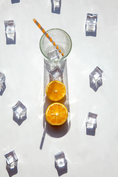 istock An empty glass with a big shadow around it, ice cubes and orange slices on a white background. Solar photography. 1312344572