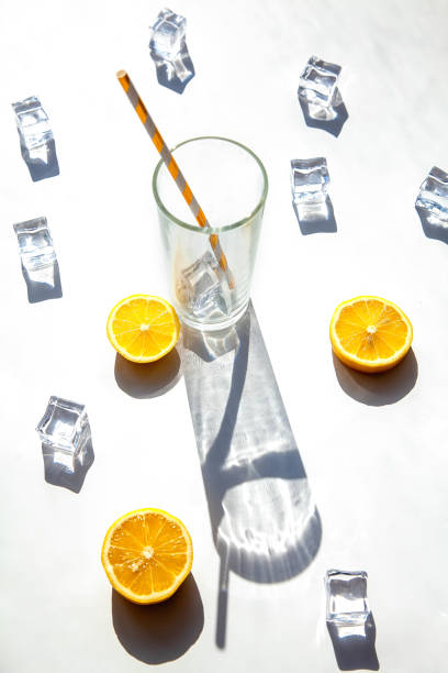 istock An empty glass with a big shadow around it, ice cubes and orange slices on a white background. Solar photography. 1312344585
