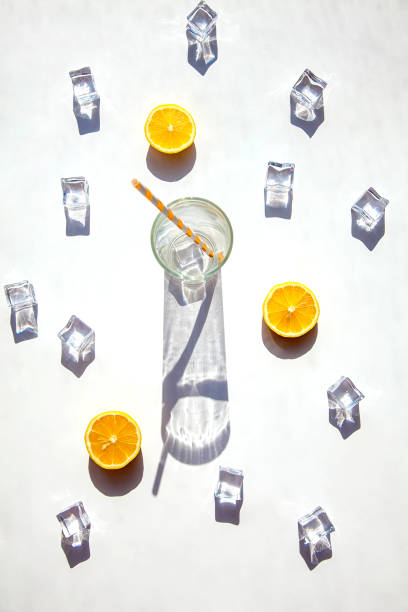 istock An empty glass with a big shadow around it, ice cubes and orange slices on a white background. Solar photography. 1312344588