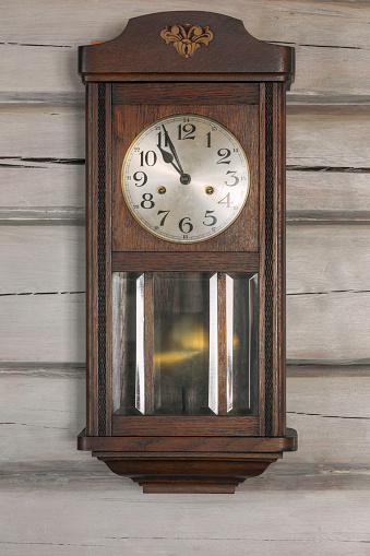 An old fashioned wooden and metal clock, telling the time at just after 4 o'clock.  Vertical.