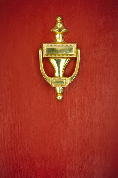 A gold colored door knocker on a red painted door.