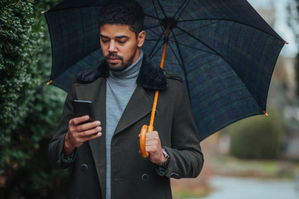 istock Businessman with umbrella texting to client on smartphone 1312345607
