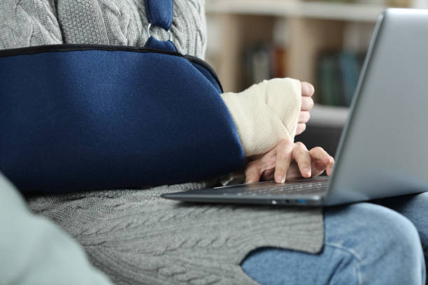 mujer con brazo roto usando cabestrillo usando computadora portátil - arm sling fotografías e imágenes de stock