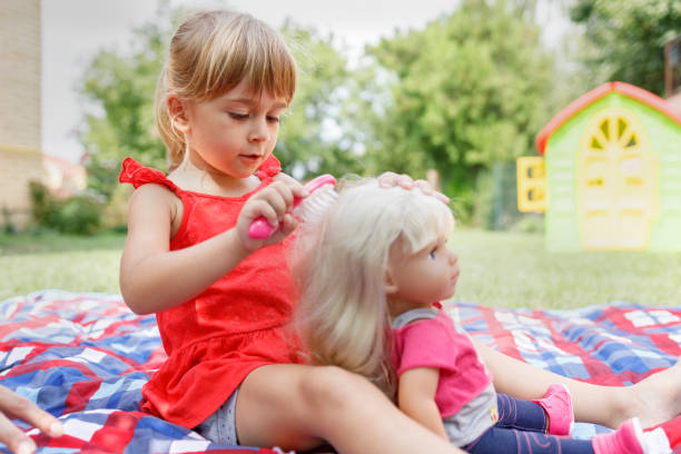 Girl brushing her doll's hair Child sitting outdoors on a blanket and using comb for her doll's hair girl playing with doll stock pictures, royalty-free photos & images