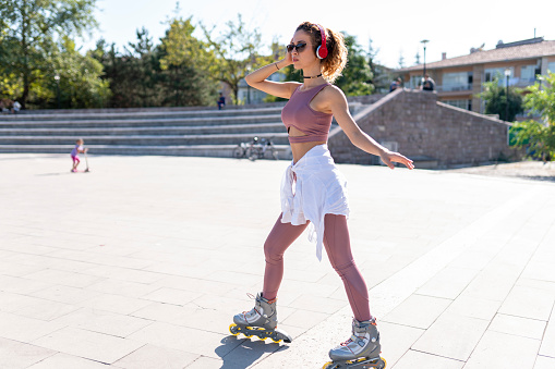 Young fit woman on roller skates riding outdoors on urban street with open arms. Smiling woman with rollerblading on sunny day