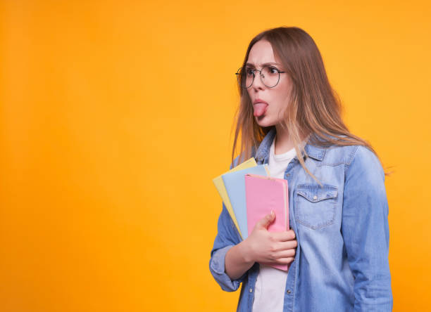 istock Cute funny student with books shows her tongue aside 1312348136