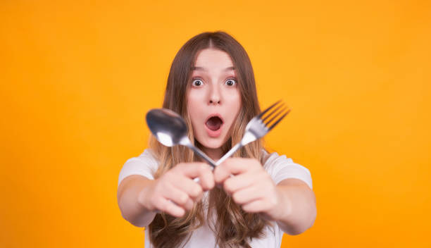 istock Surprised girl holds cross fork and spoon in her hands. 1312349074