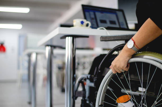 mujer con máscara facial sentada en silla de ruedas trabajando en oficina moderna - physical impairment wheelchair disabled accessibility fotografías e imágenes de stock