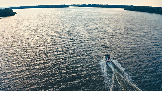 Photo from a drone above a river with a fast driving speedboat while sunset. Aerial view of driving powerboat on lake.