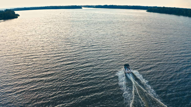 Photo from a drone above a river with a fast driving speedboat while sunset. Aerial view of driving powerboat on lake. Photo from a drone above a river with a fast driving speedboat while sunset. Aerial view of driving powerboat on lake. racing boat photos stock pictures, royalty-free photos & images