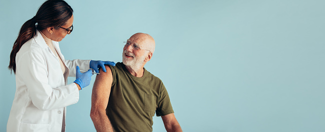 Senior man getting vaccine dose from a doctor. Doctor giving vaccine to a senior man on blue background.