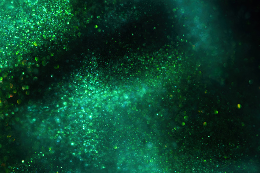 Abstract green background with tints of gold sparkles. Golden bokeh streaks on a green background with dark spots