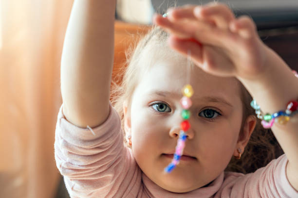 A little girl is engaged in needlework, making jewelry with her own hands, stringing multi-colored beads on a thread.