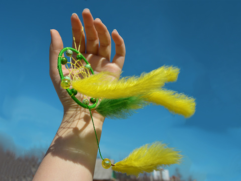 The yellow-green dreamcatcher is fluttering in the wind in a woman's hand. Copyspace for the text.