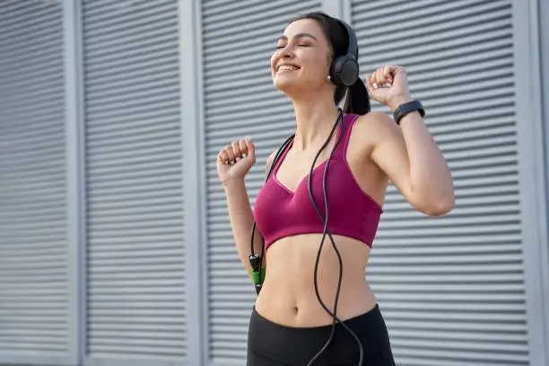 Pretty young lady with closed eyes enjoying music while exercising outdoors. Sport concept. Copy space