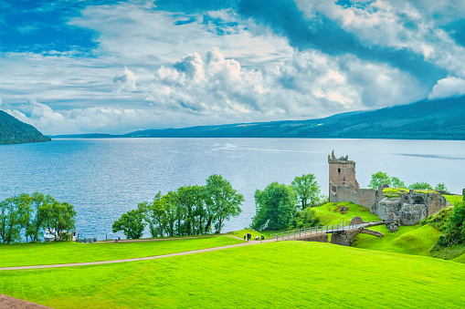 People visit Urquhart castle on the shores of Loch Ness in Scotland on a cloudy day.