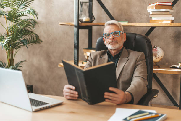 istock Studying in old age. Dreaming mature man with a book at the table. An answer to a disturbing question 1312363483