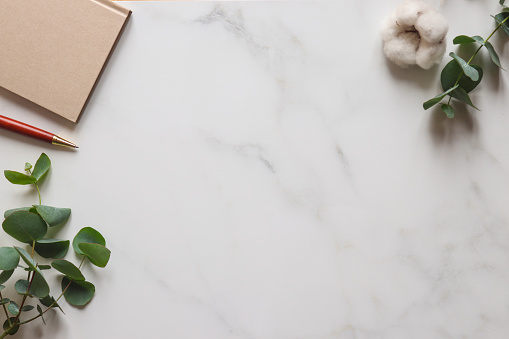 Marble minimal table desk. Eucalyptus leaves, cotton flower, notepad and pen. Template for design or invitation, copy space. Top view, flat lay. Natural style.