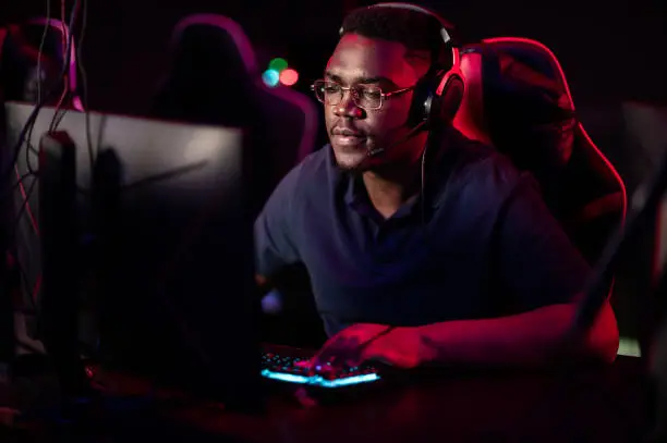 Photo of An african guy wearing headphones and glasses leads an online stream during the computer games championship