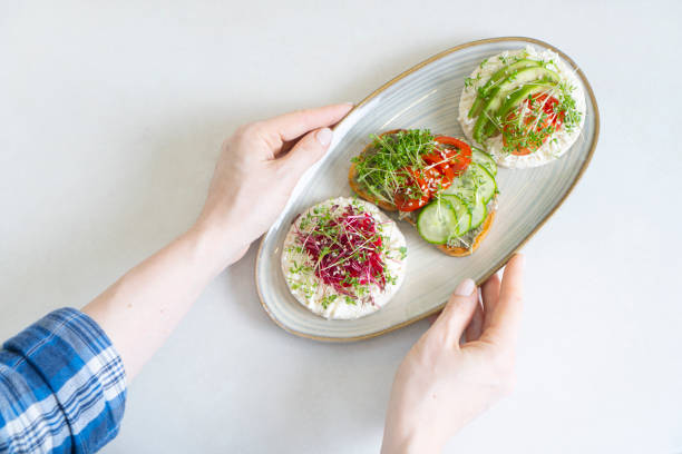 istock Female hands holding a plate with toasts made with fresh microgreen sprouts. View above. 1312369175