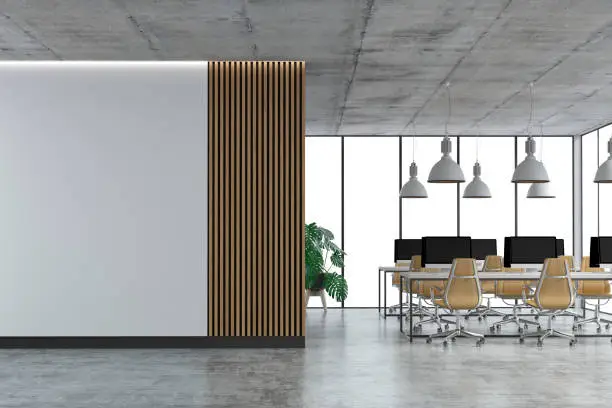 Empty office interior with a large empty light hardwood and partly white wall and copy space on concrete floor. Wordesks, lighting, potted plant and computer equipment with windows in background. 3D rendered image.