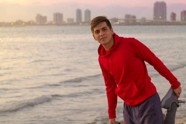 Young athletic man running, doing Exercises and training for marathon outdoors at Miami Beach, Florida, USA Sport fitness Young latin athletic man stretching while running, doing Exercises and training for marathon outdoors at the beach during a gold sunset / sunrise at Key Biscayne, Miami Beach, Miami, Florida, United States of America. He's wearing a nice red sweater and blue short training pants.

During the Covid-19 Pandemic illness all the gym clubs are closed and the people as this young guy need to training outside.

Healthy lifestyle concept. miami marathon stock pictures, royalty-free photos & images