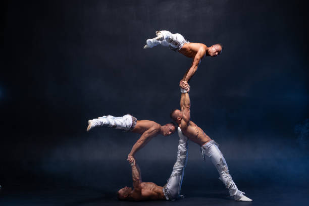 quatre hommes musculaires exécutent des tours acrobatiques difficiles sur le studio noir - acrobate photos et images de collection