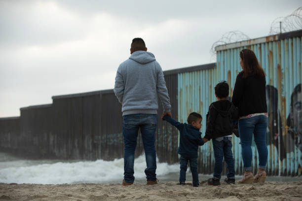 USA Mexico Border Wall Tijuana, Baja California, Mexico - April 11, 2021: A family stands in front of the USA Mexico border wall. immigrant stock pictures, royalty-free photos & images