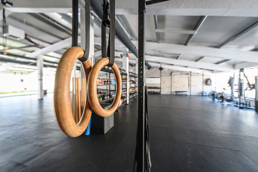 Wide angle view with focus on foreground gymnastic rings of unoccupied open plan gym with exposed ceiling and vast space for workouts.
