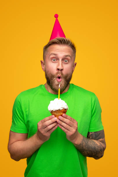 istock Funny male blowing candle on cupcake 1312386396