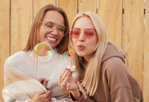 Cheerful girlfriends in stylish sunglasses blowing soap bubbles