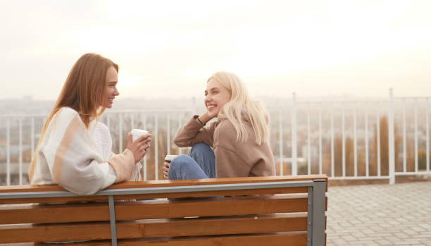 istock Cheerful girlfriends with takeaway coffee chatting on bench 1312386456