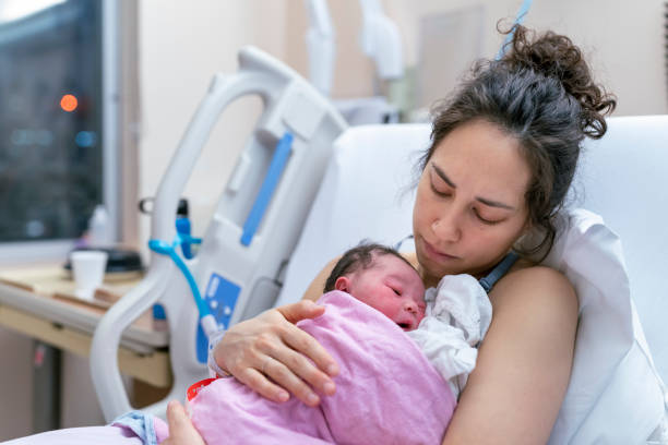 Mixed Race Mother Snuggling Newborn After Delivery A beautiful and relaxed ethnic mother is snuggling her newborn and affectionately holding her in the hospital after delivery. Skin to skin bonding concept. new baby stock pictures, royalty-free photos & images