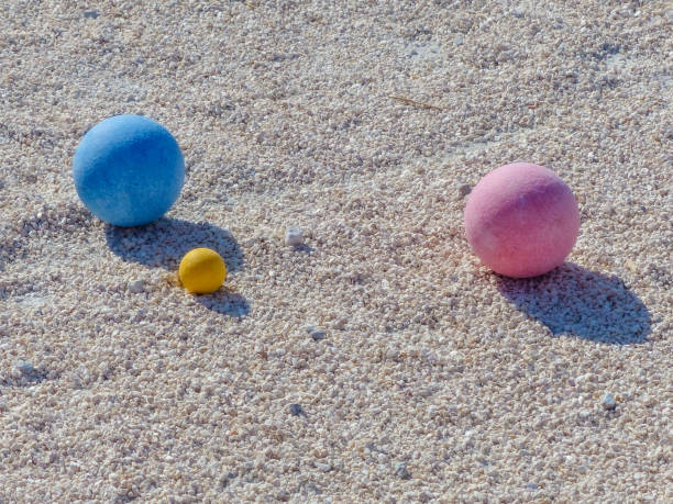 Petanque precision shooting competition moment with metal balls hitting target in sand, dust flying on impact. Focus on accuracy and dynamic play.