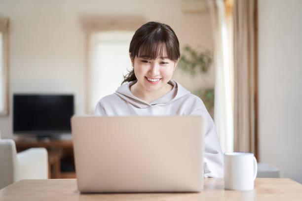 asiatische frau, die einen computer mit einem lächeln im wohnzimmer - hausfrau fotos stock-fotos und bilder