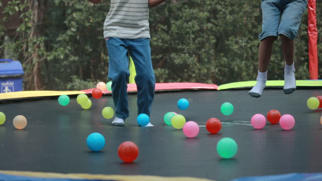 Children wearing socks jumping on the trampoline with colorful balls.
