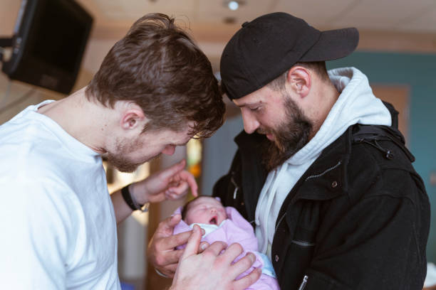 Two Men Holding Newborn Baby Together At Hospital Two caucasian men in their thirties are affectionally holding and looking at a newborn baby lovingly. surrogacy stock pictures, royalty-free photos & images