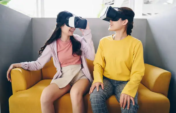 Photo of Two young Asian women wearing virtual reality glasses and playing video games together.