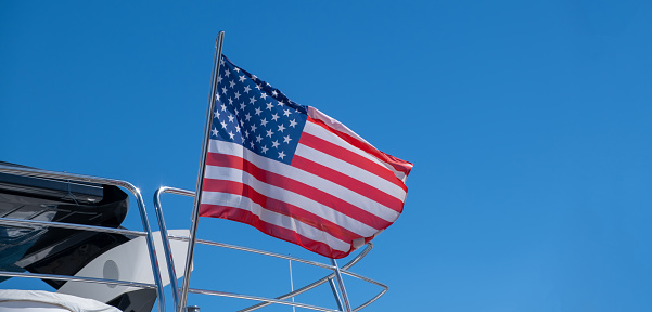United states of America flag waving on yacht stern. Luxury boat moored at marina in Athens Greece. Blue sky background, copy space.