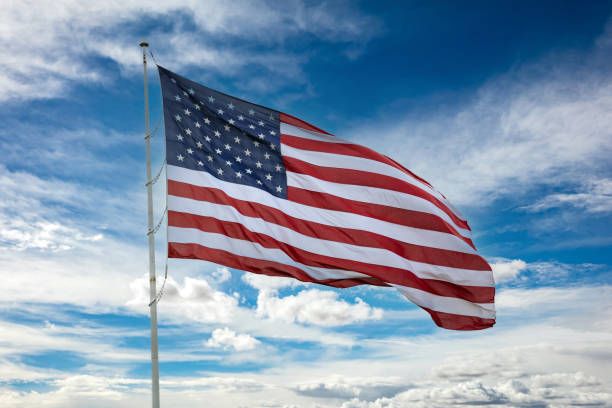 istock USA flag on a pole waving against blue cloudy sky background. 1312409209