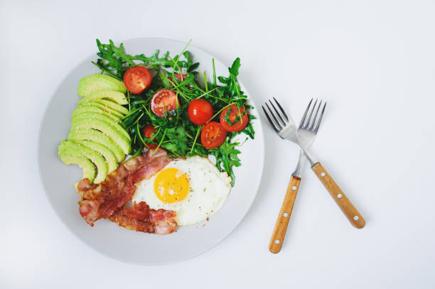 istock tasty breakfast - fried egg and bacon served with arugula tomato salad and fresh avocado on white plate 1312412086