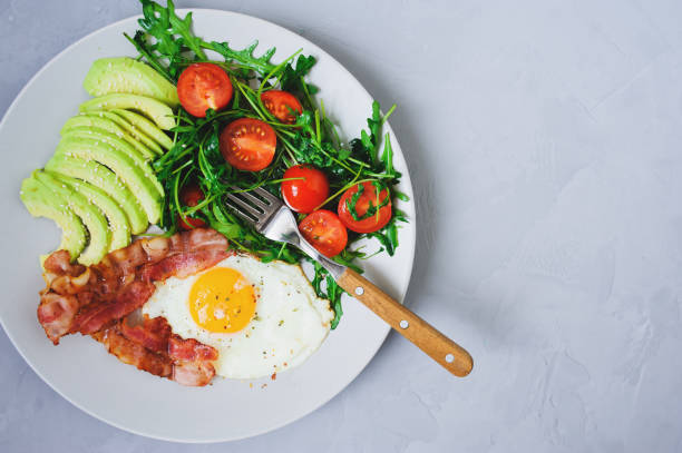 istock tasty breakfast - fried egg and bacon served with arugula tomato salad and fresh avocado on white plate 1312412088