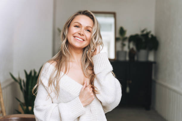 blonde smiling woman 35 year clean fresh face and hands with long hair in cozy knitted cardigan at bright interior - attractive female indoors lifestyles clean imagens e fotografias de stock