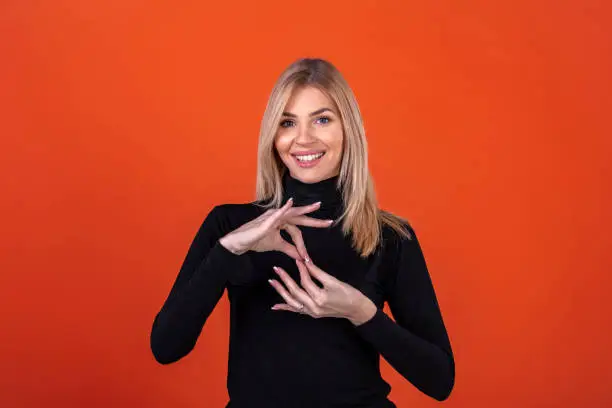 Portrait Of One Smiling Woman Using Sign Language While Standing Over Red Background.