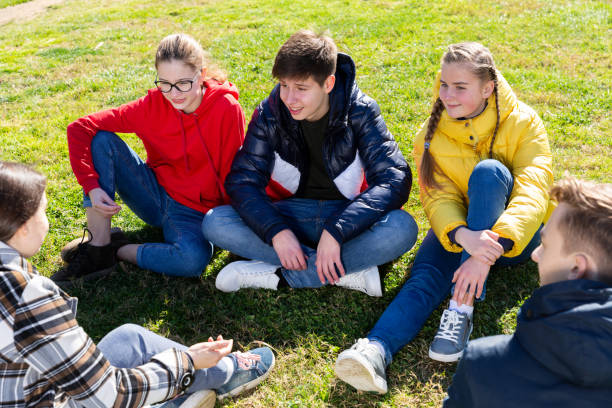 istock Cheerful teens sitting on green lawn and talking 1312416506