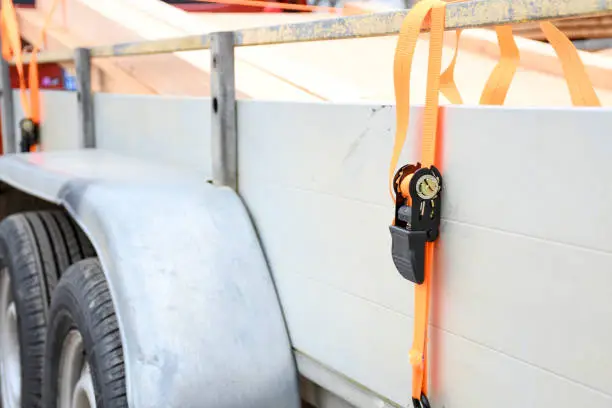 Photo of Trailer strop or strap in orange nylon and metal, object helping for holding stuff , storage and transport for safty and security.