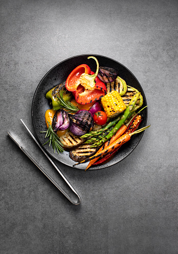 Grilled vegetables served on a plate with BBQ tongs, ready to eat outdoor picnic dish, top down view