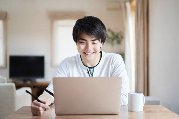 homme asiatique parlant en ligne avec un sourire - internet student business men photos et images de collection